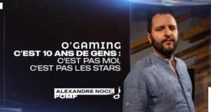 Homme en chemise bleue devant fond sombre.