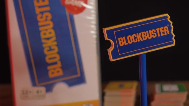 découvrez pourquoi blockbuster: the game est l’expérience ludique à ne Enseigne bleue Blockbuster devant emballage.