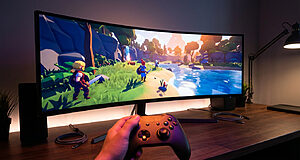 Hand holding gamepad, playing vibrant PS2-inspired 3D game on a curved monitor in a modern, minimalist setup.