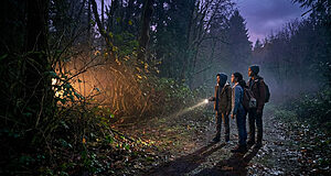 Enfants explorant forêt sombre avec lampes torches.