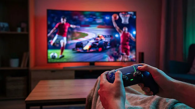 Gaming Thrills: Controller in Focus, Sports Montage Hands hold a sleek Xbox controller with glowing accents. Blurred TV shows dynamic sports: soccer, racing, basketball. Energetic screen light.