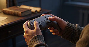 Hands hold a sleek game controller in warm light. Blurred background with an old book and parchment hints at learning and a hopeful mood.