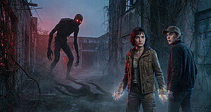 A young woman with glowing hands and a man face a red-eyed monster in a foggy, derelict lab with overgrown vines.