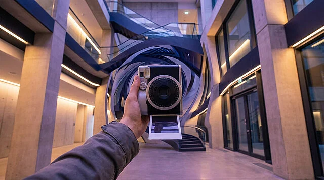 surreal instant camera warps modern architecture Main tenant un appareil photo dans un hall moderne.