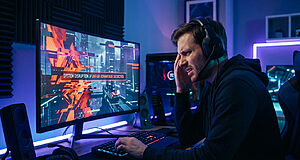 A frustrated male gamer in a headset reacts to 'UNFAIR ADVANTAGE DETECTED' on his monitor in a dimly lit, futuristic room.
