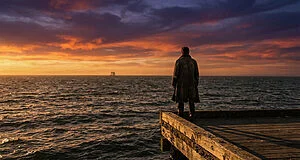 Figure on a weathered pier looking at a vast, turbulent ocean under a dramatic orange and purple sunset sky, with a distant sailing ship.