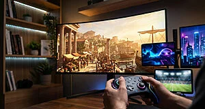 Mains tenant une manette Xbox lumineuse. Grand écran incurvé affiche un jeu antique, accompagné de deux écrans secondaires.