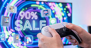 Mains tenant une manette PS5 DualSense devant un écran affichant "90% SALE" en néon et des jeux rétro.