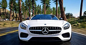 Vue frontale d'une Mercedes-Benz AMG GT blanche sur une route asphaltée, bordée de grands arbres. Le ciel est bleu.