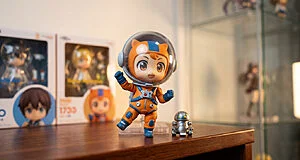 Figurine Nendoroid Esquie portant une combinaison d'astronaute orange, accompagnée d'un petit robot sur une table en bois.