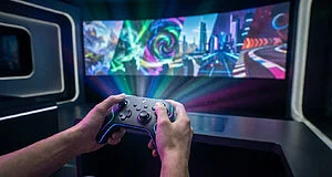 Mains d'un joueur tenant une manette illuminée devant un écran incurvé diffusant un jeu vidéo futuriste coloré.