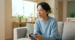 Une femme d'une trentaine d'années assise sur un canapé, tenant une manette de console et jouant aux jeux vidéo.