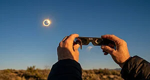 Personne regardant une éclipse solaire avec des lunettes de protection certifiées ISO 12312-2 sous un ciel clair.