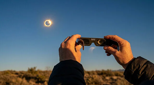 Éclipse solaire : vue sécurisée avec lunettes certifiées Personne regardant une éclipse solaire avec des lunettes de protection certifiées ISO 12312-2 sous un ciel clair.