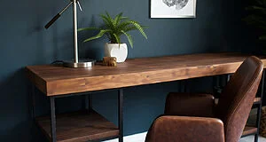 Un bureau en bois sombre avec un cadre métallique noir, une chaise en cuir marron, une lampe et une plante verte sur un mur bleu.