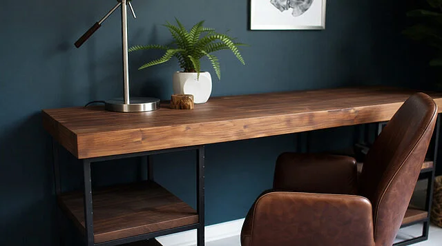 Bureau contemporain pour réflexion et innovation Un bureau en bois sombre avec un cadre métallique noir, une chaise en cuir marron, une lampe et une plante verte sur un mur bleu.