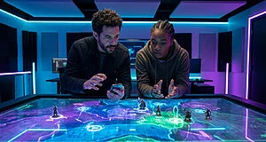 Deux personnes jouent à un jeu de stratégie sur une table tactile lumineuse dans une salle au néon bleu et violet.