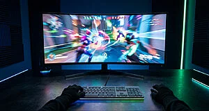 Vue subjective d'un joueur utilisant un écran gaming incurvé affichant un jeu rapide avec un éclairage néon.