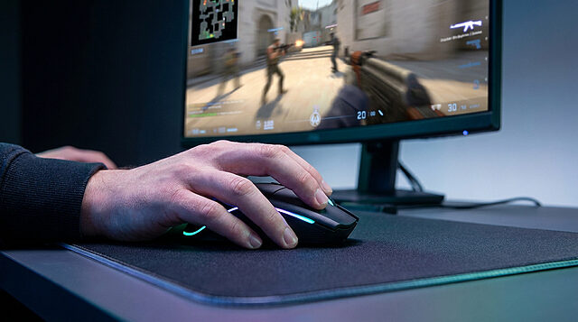 Main d'un joueur posée sur une souris gaming devant un écran affichant une partie intense de Counter-Strike 2.