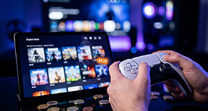 Mains tenant une manette PS5 devant une tablette affichant des jeux avec une étiquette de prix à 0,99 €.