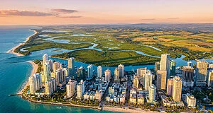 Vue aérienne panoramique d'une métropole côtière moderne inspirée de Vice City au coucher du soleil.