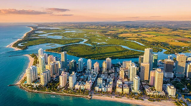 GTA 6 : Aperçu de la nouvelle carte de Vice City Vue aérienne panoramique d'une métropole côtière moderne inspirée de Vice City au coucher du soleil.