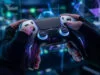 Mains portant des gants techniques tenant une manette futuriste devant un écran rempli de données numériques.