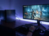 Une personne joue à un jeu vidéo sur PC avec un clavier, une souris et une console PS3 posée sur le bureau éclairé.