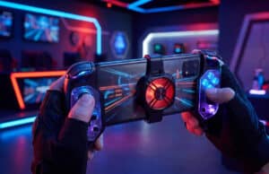 Meilleurs accessoires smartphone gaming 2026 : jouez comme un pro Mains tenant un smartphone avec manette intégrée et ventilateur de refroidissement dans une salle gaming néon.