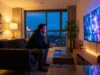 Un homme joue aux jeux vidéo sur sa télévision en streaming depuis son canapé dans un salon moderne.