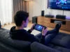Jouer à la PS5 sur ton Steam Deck grâce au cloud avec Asobi Un jeune homme détendu sur un canapé jouant à la PS5 sur son Steam Deck via l'application Asobi.