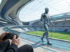 Robot humanoïde au Mexique : pilote le futur à la manette Une personne tenant une manette de jeu contrôle un robot humanoïde argenté marchant dans un stade futuriste.