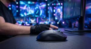 Gros plan sur une souris gaming Logitech G Pro X Superlight 3 posée sur un tapis, avec un joueur en arrière-plan.