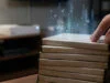 Fin des jeux physiques PlayStation : le choc de 2028 Une main touche une pile de boîtiers de jeux vidéo avec un effet de particules numériques s'en échappant.