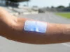 Capteur papier transpiration : l’énergie du futur pour le suivi Bras d'un athlète portant un patch en papier bleu sur la peau, sur une piste d'athlétisme en arrière-plan.