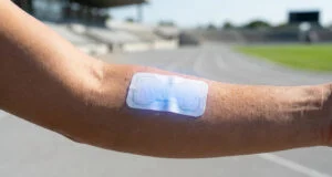 Bras d'un athlète portant un patch en papier bleu sur la peau, sur une piste d'athlétisme en arrière-plan.
