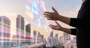 Une personne manipulant une interface holographique numérique devant un paysage urbain moderne au coucher du soleil.