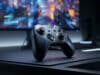 Quelle manette choisir pour jouer sur PC en 2026 ? Une manette de jeu moderne posée sur un bureau devant un écran affichant un jeu vidéo avec des lumières bleues.