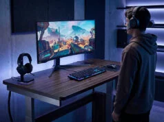 Meilleur bureau assis debout gaming 2026 : l’ergonomie au service du jeu Un joueur debout devant un bureau réglable avec un écran ultra-large dans une salle de jeu moderne.