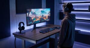 Un joueur debout devant un bureau réglable avec un écran ultra-large dans une salle de jeu moderne.