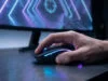 Gros plan sur une main de gamer utilisant une souris rétroéclairée devant un écran de jeu avec un viseur.