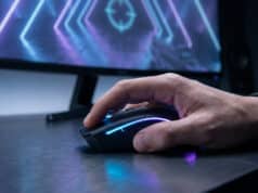 Optimisez vos réglages souris sur Valorant pour mieux viser Gros plan sur une main de gamer utilisant une souris rétroéclairée devant un écran de jeu avec un viseur.