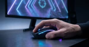 Gros plan sur une main de gamer utilisant une souris rétroéclairée devant un écran de jeu avec un viseur.