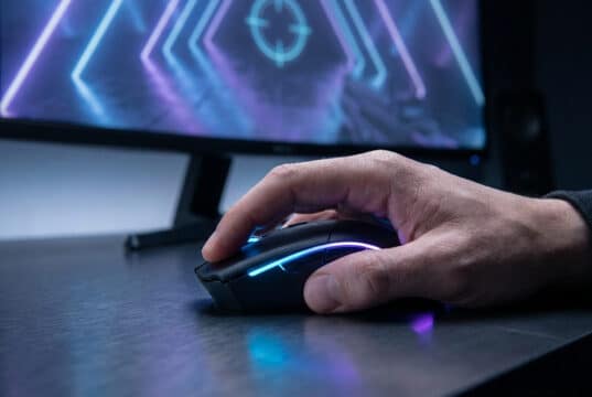 Gros plan sur une main de gamer utilisant une souris rétroéclairée devant un écran de jeu avec un viseur.