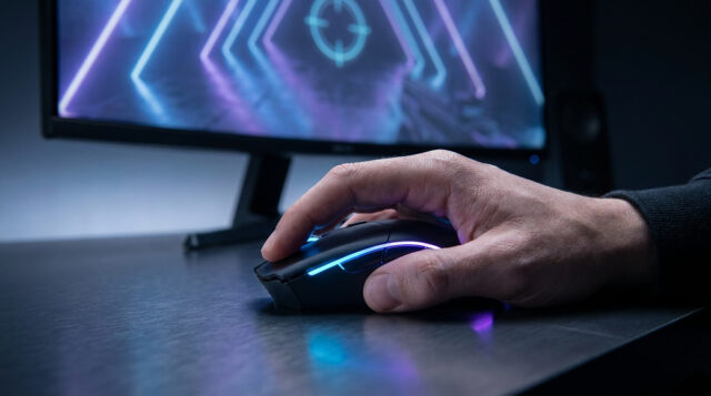 Optimisez vos réglages souris sur Valorant Gros plan sur une main de gamer utilisant une souris rétroéclairée devant un écran de jeu avec un viseur.