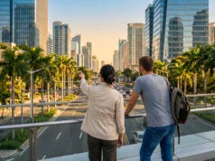 Deux personnes observent une ville moderne depuis une passerelle piétonne en surplomb d'une avenue.