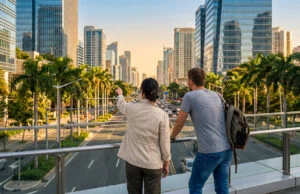 Deux personnes observent une ville moderne depuis une passerelle piétonne en surplomb d'une avenue.