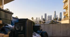 Un boîtier de PC gaming noir posé au sol près de poubelles, avec les gratte-ciels de Los Angeles en arrière-plan.