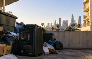 Un boîtier de PC gaming noir posé au sol près de poubelles, avec les gratte-ciels de Los Angeles en arrière-plan.