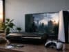 Une console PS5 et une PS3 posées sur un bureau, avec un jeu rétro en cours de lecture sur l'écran en arrière-plan.